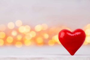 A red heart in the foreground with many light blurs behind it.